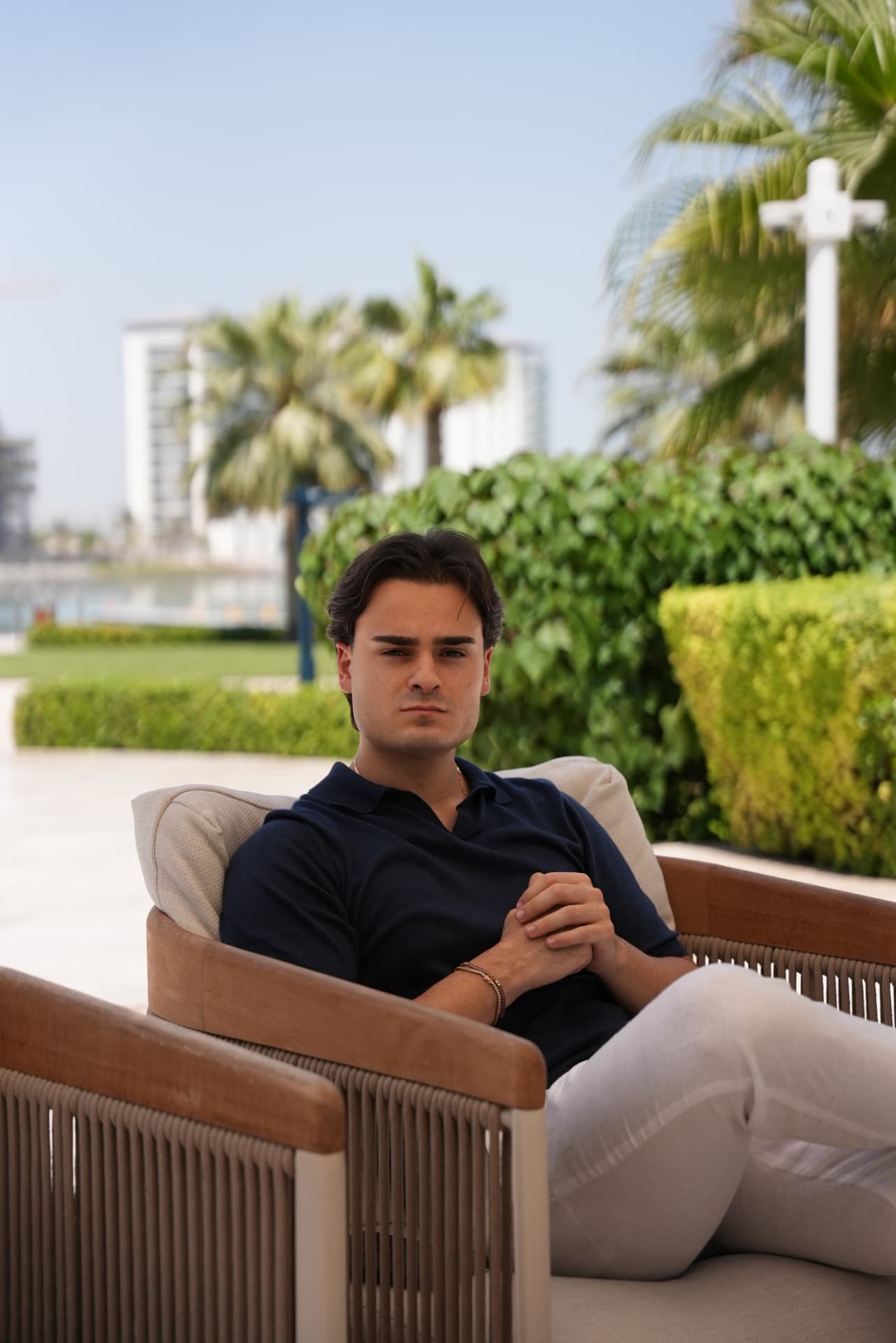 Antonio Romano seduto in una poltrona da esterno, palme e architettura di Dubai sullo sfondo